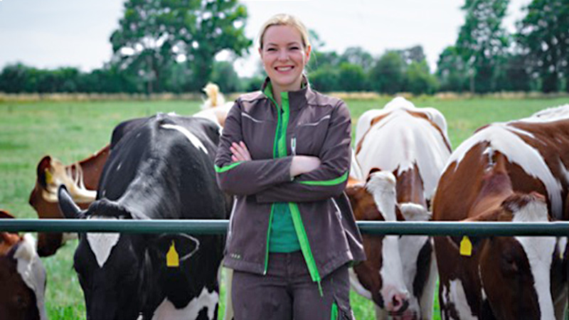 Ein Bild, das eine Landwirtin zeigt, die vor einer Weide mit Kühen steht