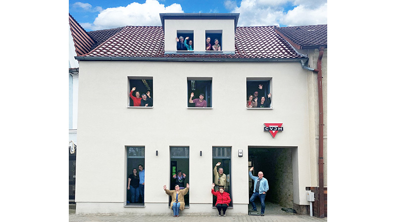 Ein Bild, das ein Haus mit vielen winkenden Menschen an den Fenstern zeigt