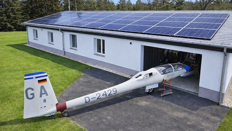 Bild zeigt ein Segelflugzeug vor einer Werkstatteinfahrt.