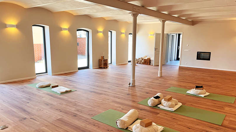 Das Bild zeigt eine Halle mit Yogamatten auf dem Holzboden.