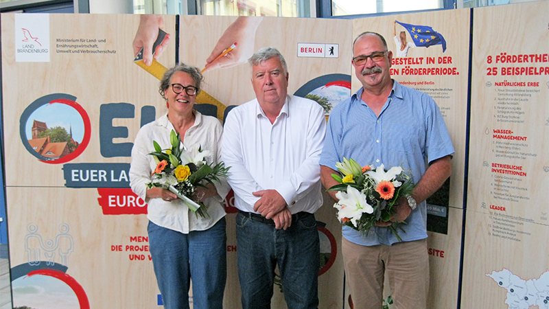 Drei Personen stehen vor einer Ausstellungswand.